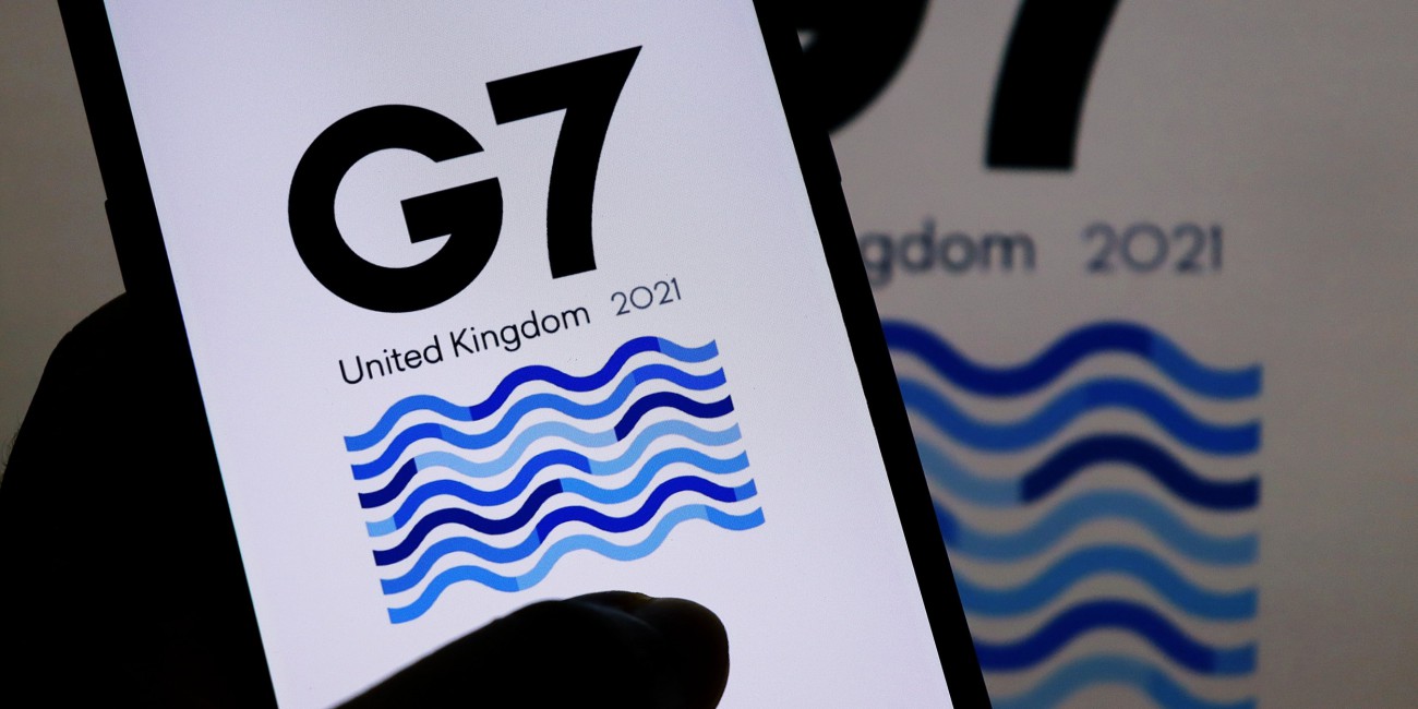 Hand holding mobile phone showing G7 2021 logo