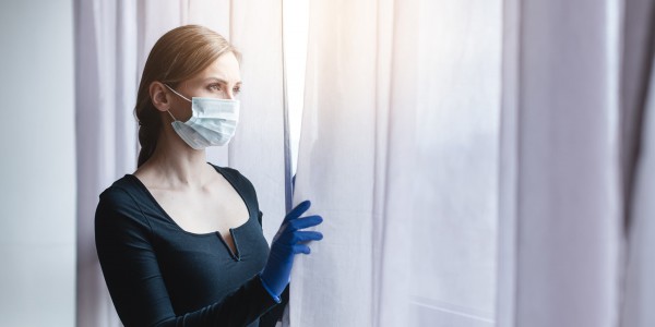 Woman wearing a facemask and rubber gloves peering through curtains